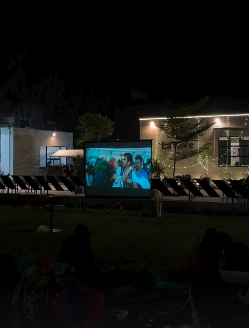 Outdoor movie screening setup with a large projection screen, comfortable seating arrangements, and ambient lighting creating a cozy cinematic environment under the night sky