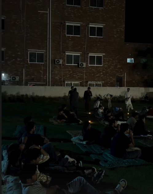 Outdoor movie screening setup with a large projection screen, comfortable seating arrangements, and ambient lighting creating a cozy cinematic environment under the night sky