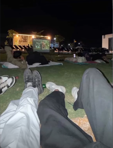 Outdoor movie screening setup with a large projection screen, comfortable seating arrangements, and ambient lighting creating a cozy cinematic environment under the night sky