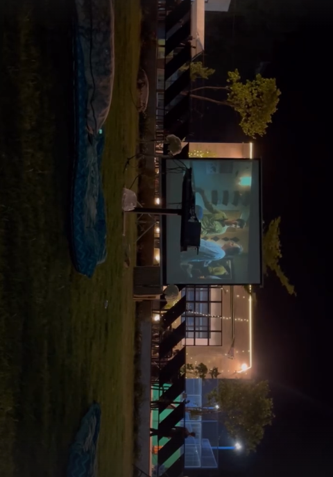 Outdoor movie screening setup with a large projection screen, comfortable seating arrangements, and ambient lighting creating a cozy cinematic environment under the night sky
