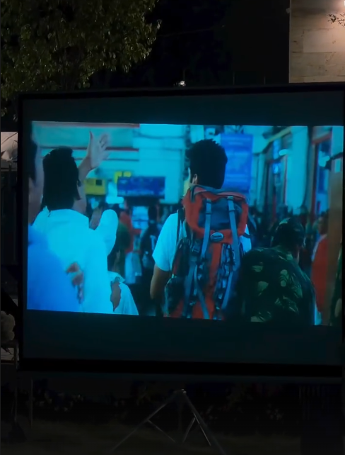 Outdoor movie screening setup with a large projection screen, comfortable seating arrangements, and ambient lighting creating a cozy cinematic environment under the night sky